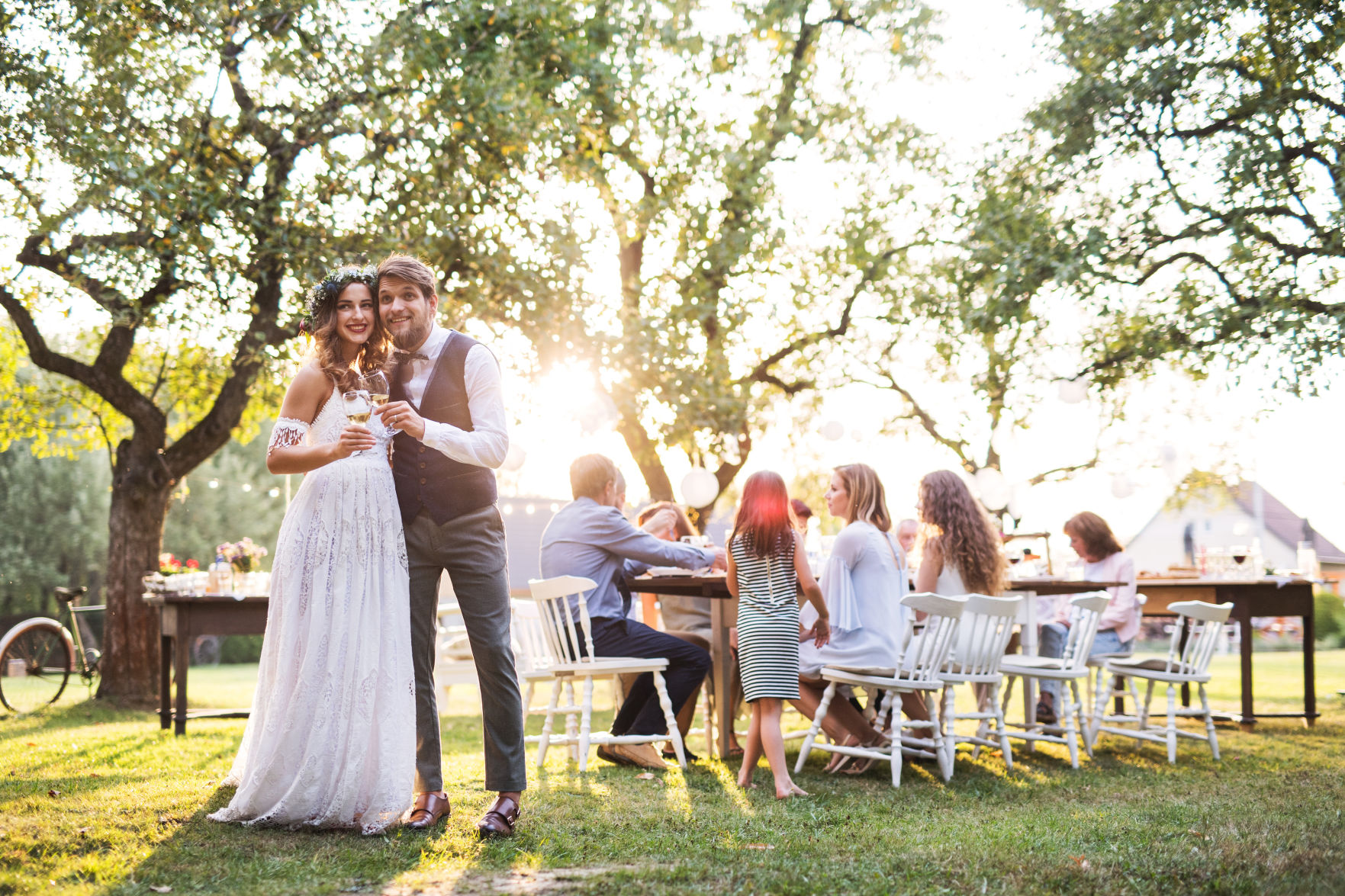 Bride and groom clinking glasses at wedding reception outside in the backyard.